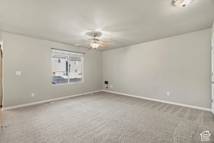 Neutral-toned interior space featuring wall-to-wall carpeting, a multi-blade ceiling fan with integrated lighting, and a single-pane window