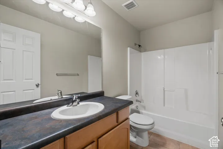 Bathroom featuring a wood-finish vanity with a dark-toned countertop, integrated oval sink, full-width mirror, and a tub-shower combination with a white surround