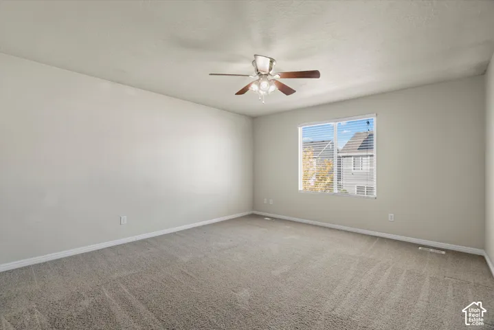 Neutral interior featuring wall-to-wall carpeting, a multi-blade ceiling fan with integrated lighting, and a window with horizontal blinds