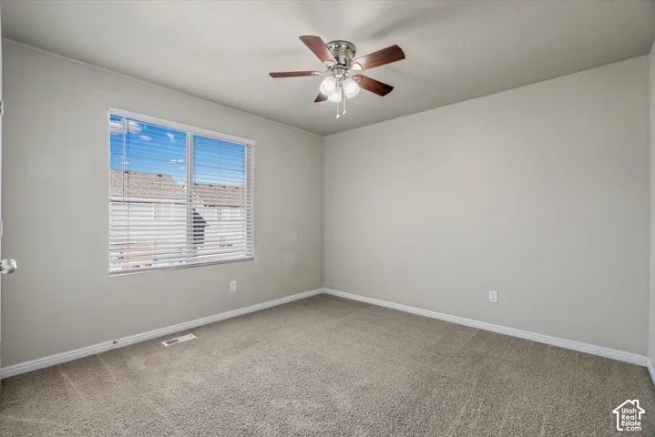 Neutral-toned interior featuring wall-to-wall carpeting, a multi-blade ceiling fan with integrated lighting, and a large window with horizontal blinds