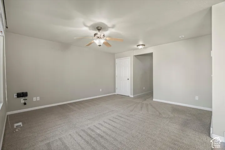 Neutral-toned interior room featuring wall-to-wall carpeting, a ceiling fan with integrated light fixture, a recessed ceiling light, and a six-panel interior door