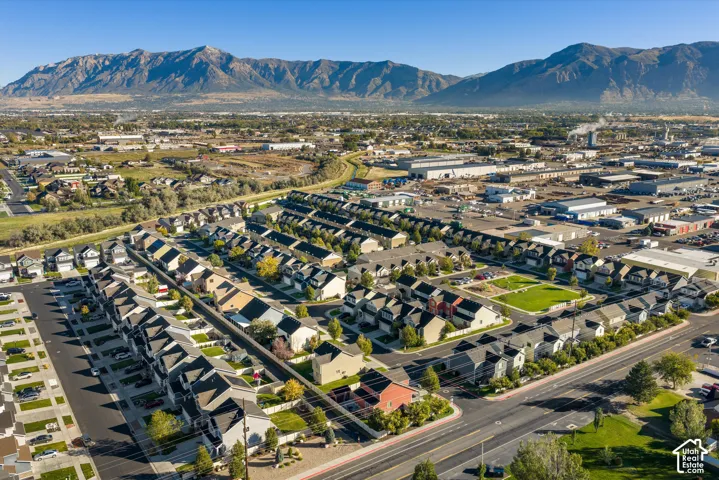 Aerial perspective of a residential development featuring uniform multi-story structures, paved street networks, integrated green spaces, and prominent mountain backdrops
