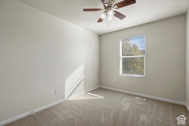 Neutral-toned interior space featuring textured wall-to-wall carpeting, a single-hung window with horizontal blinds, and a multi-blade ceiling fan with integrated lighting