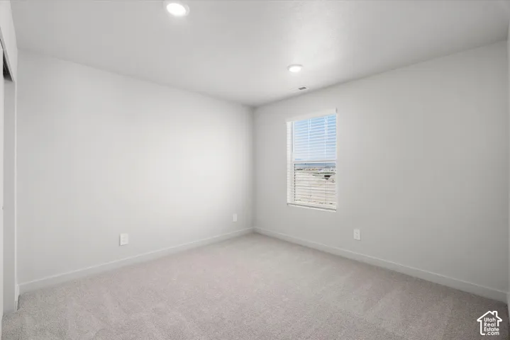 Neutral-toned interior space featuring light-colored wall-to-wall carpeting, recessed ceiling lighting, and a window with fitted horizontal blinds