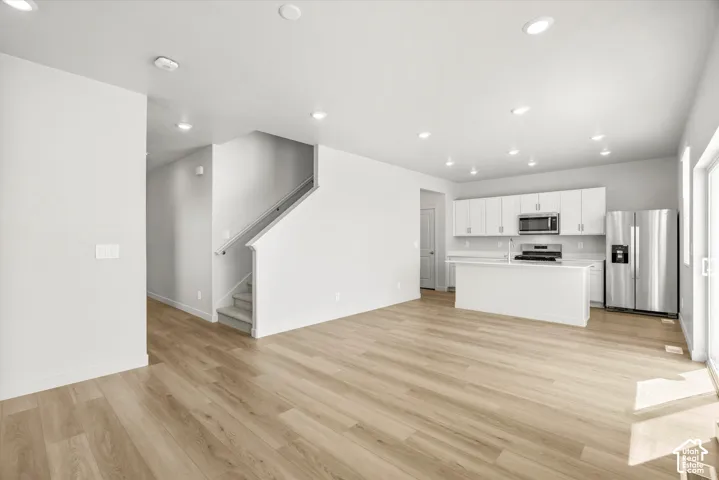 Open-concept interior featuring light wood-finish flooring, recessed lighting, kitchen island with stone-surface countertop, white cabinetry, and stainless steel appliances