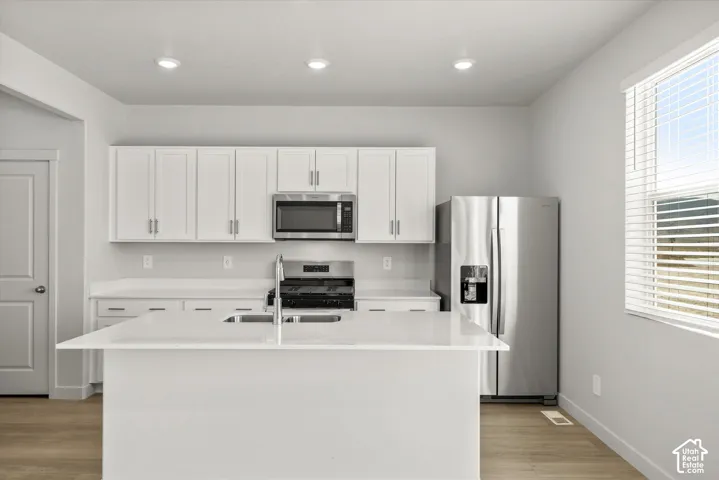 Kitchen featuring white cabinetry, solid-surface countertops, center island, stainless steel appliances, and wood-finish flooring