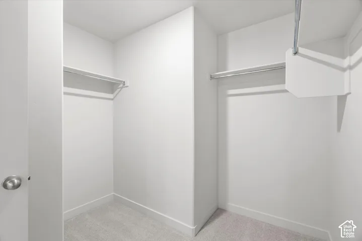 Walk-in storage space featuring neutral carpeting, white wall finishes, and dual integrated metal hanging rods with overhead shelving