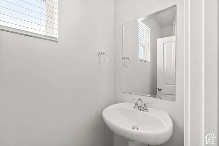 Wall-mounted mirror, pedestal sink with chrome faucet, and horizontal slatted blinds