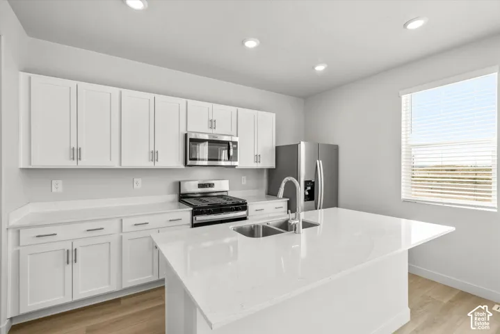 Kitchen featuring white shaker-style cabinetry, quartz countertops, central island with dual-basin stainless steel sink, stainless steel appliances, and wood-finish flooring