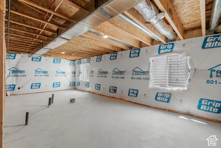 Unfinished interior space featuring exposed wood joists, concrete flooring, dual egress windows, and pre-installed plumbing rough-ins