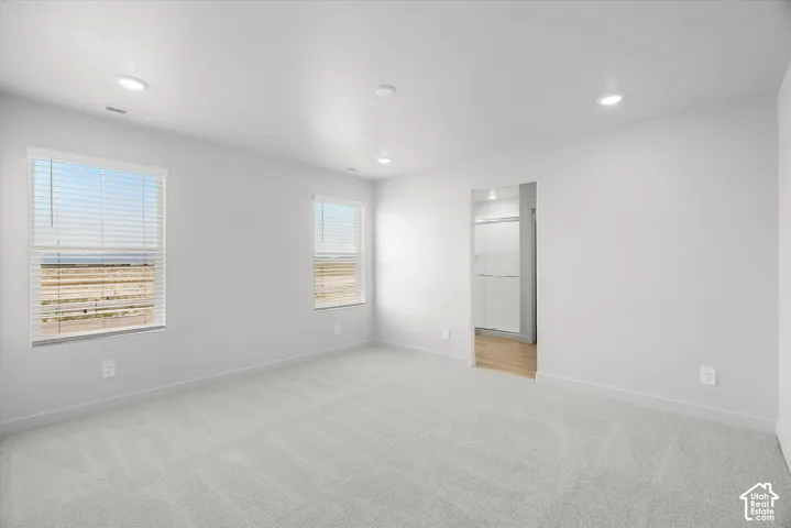 Neutral-toned interior space featuring recessed ceiling lighting, light-colored wall-to-wall carpeting, and multiple windows with integrated blinds