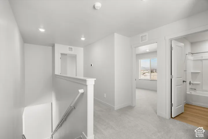 Neutral interior featuring carpeting, recessed lighting, a staircase with a white railing, and a bathroom containing a tub-shower combination with wood-finish flooring