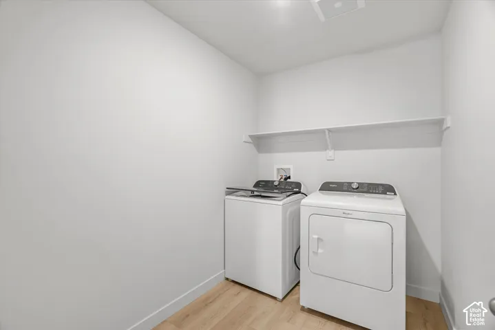 Dedicated laundry area featuring light wood-finish flooring, neutral wall paint, and an installed wall-mounted storage shelf