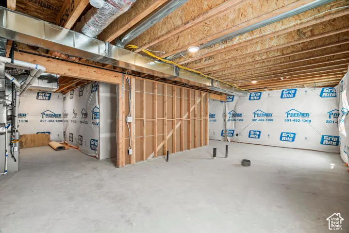 Unfinished basement featuring concrete flooring, exposed wooden ceiling joists, metal HVAC ductwork, interior wood-framed walls, and plumbing stub-outs