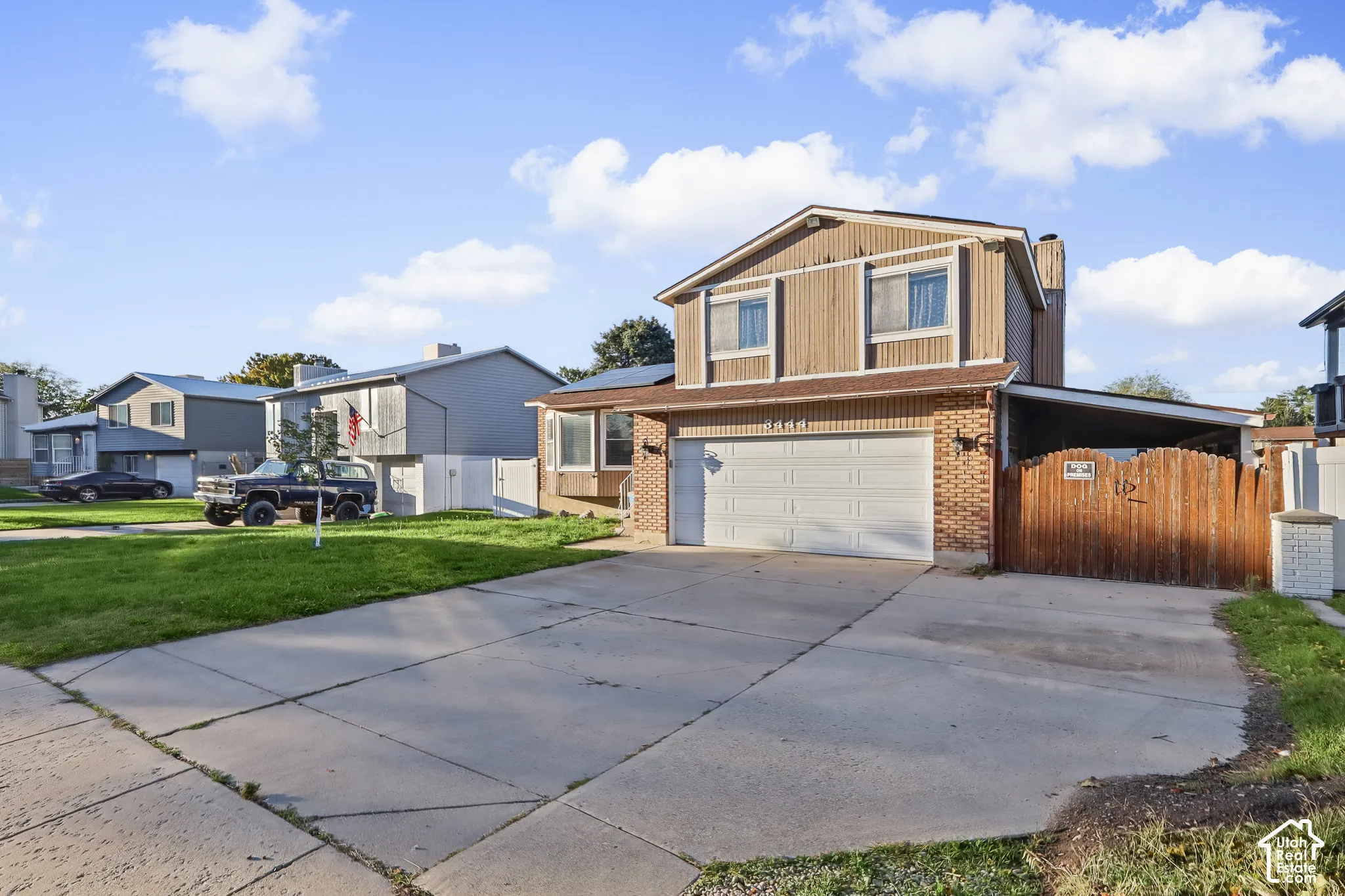 Multi-level residence with vertical siding and brick veneer exterior, two-car garage, concrete driveway, and attached wood privacy fencing