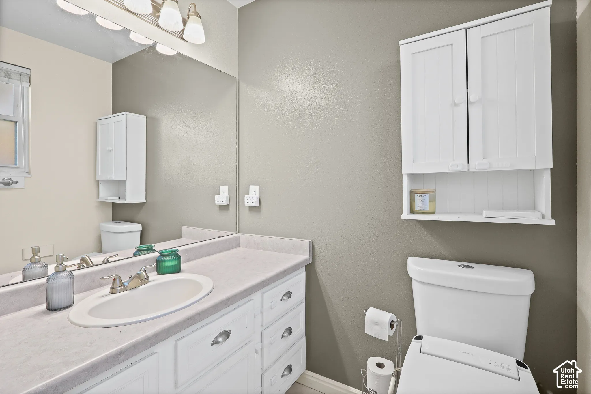 Ensuite bathroom vanity featuring white cabinetry, a molded sink, and a solid-surface countertop, complemented by a large wall-mounted mirror, multi-bulb overhead lighting, and built-in white wall cabinetry