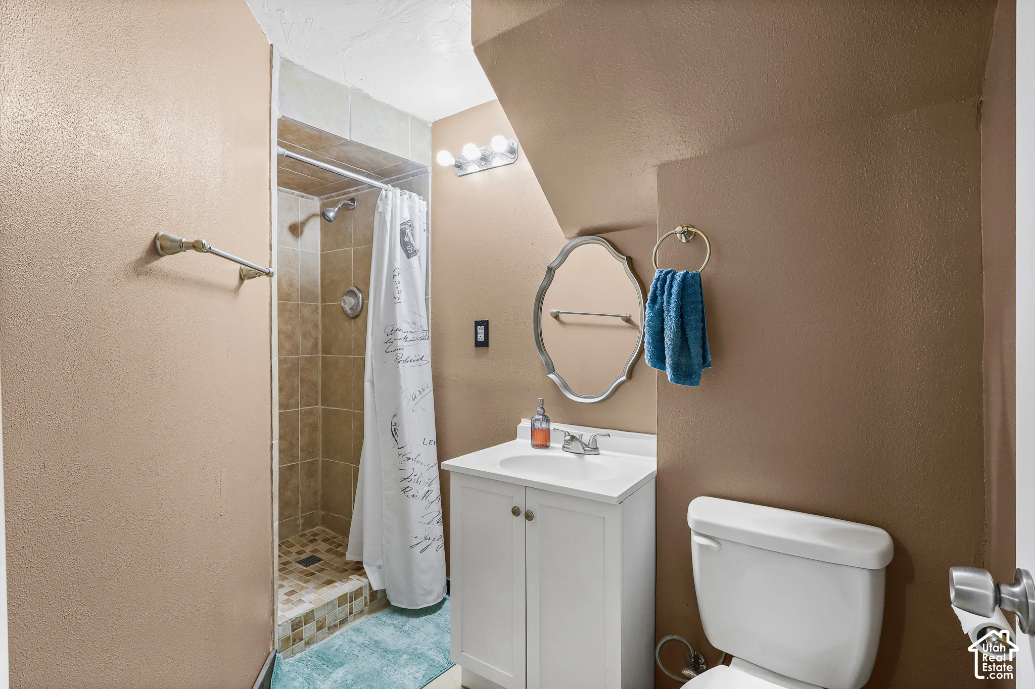 Bathroom featuring a white vanity cabinet with a stone-top integrated sink, a stall shower with tiled walls and flooring, a wall-mounted vanity light fixture, and a decorative mirror