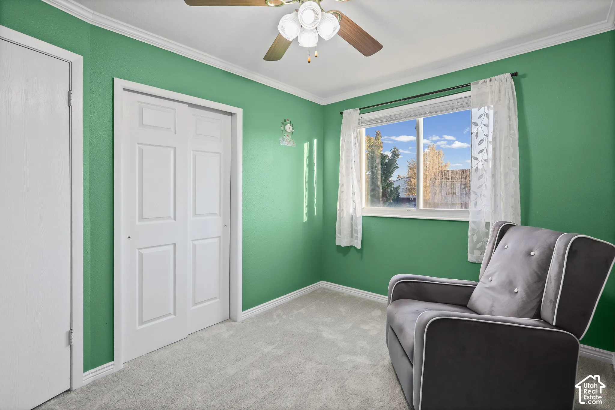 Bedroom featuring neutral carpeting, a sliding-door closet, a multi-pane sliding window, crown molding, and a ceiling fan with integrated light fixture
