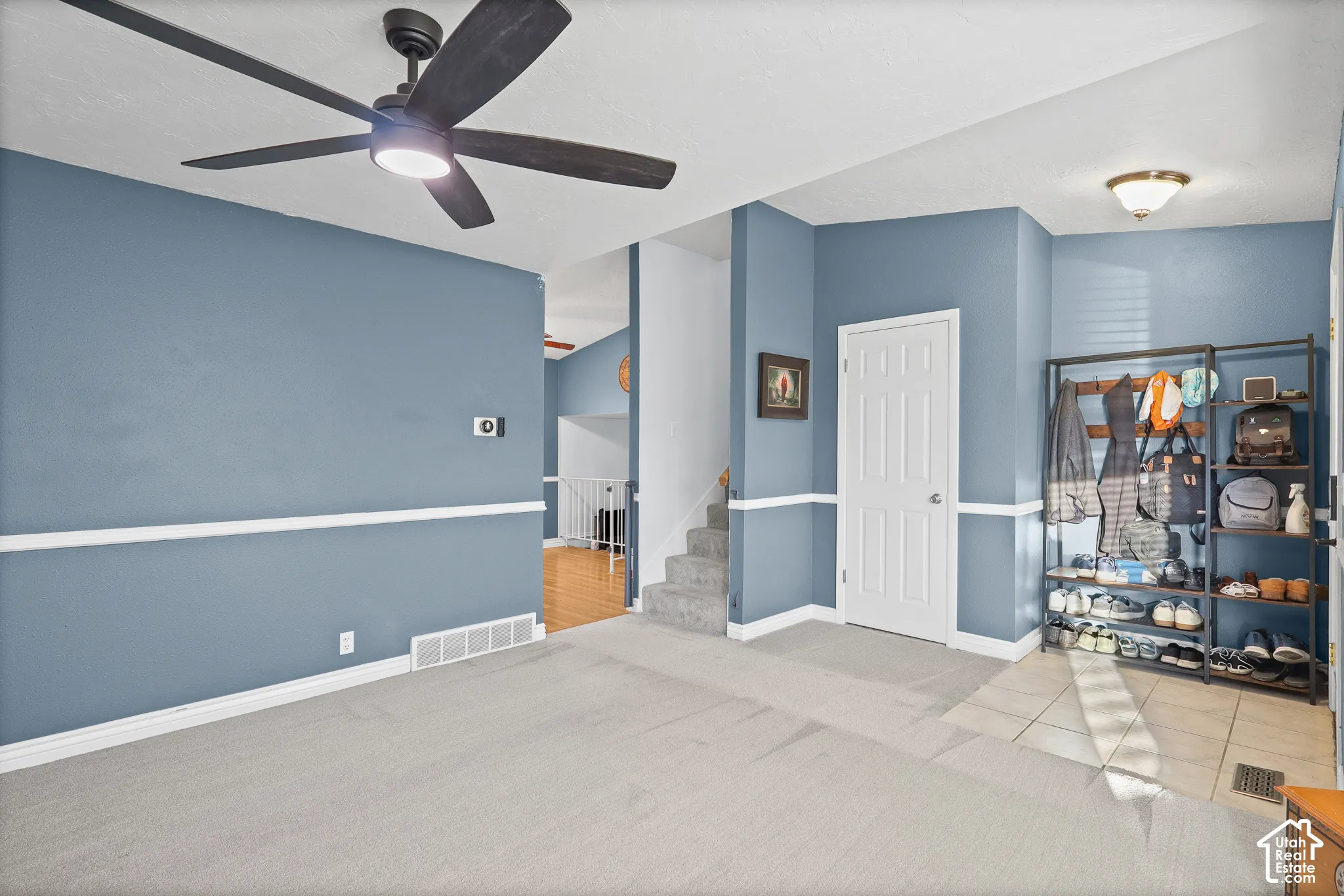 Living room space featuring grey wall-to-wall carpeting, white chair rail molding, matte black ceiling fan with integrated lighting, and a tiled entryway