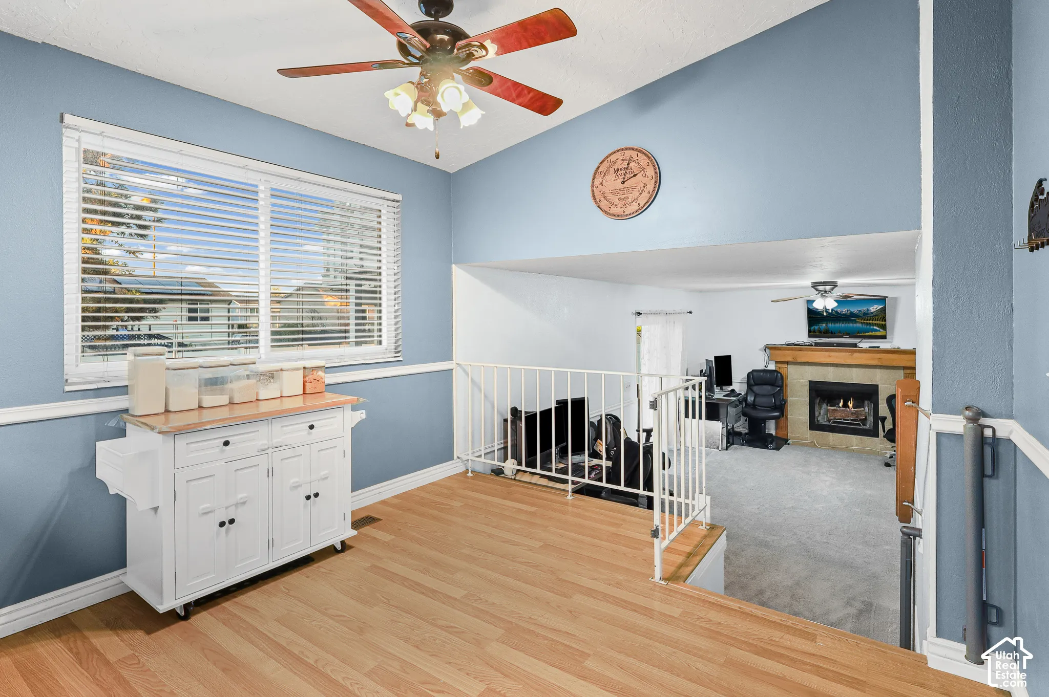 Vaulted ceilings, wood-finish flooring, metal railing, multi-pane window with horizontal blinds, and a fireplace with a wood mantel