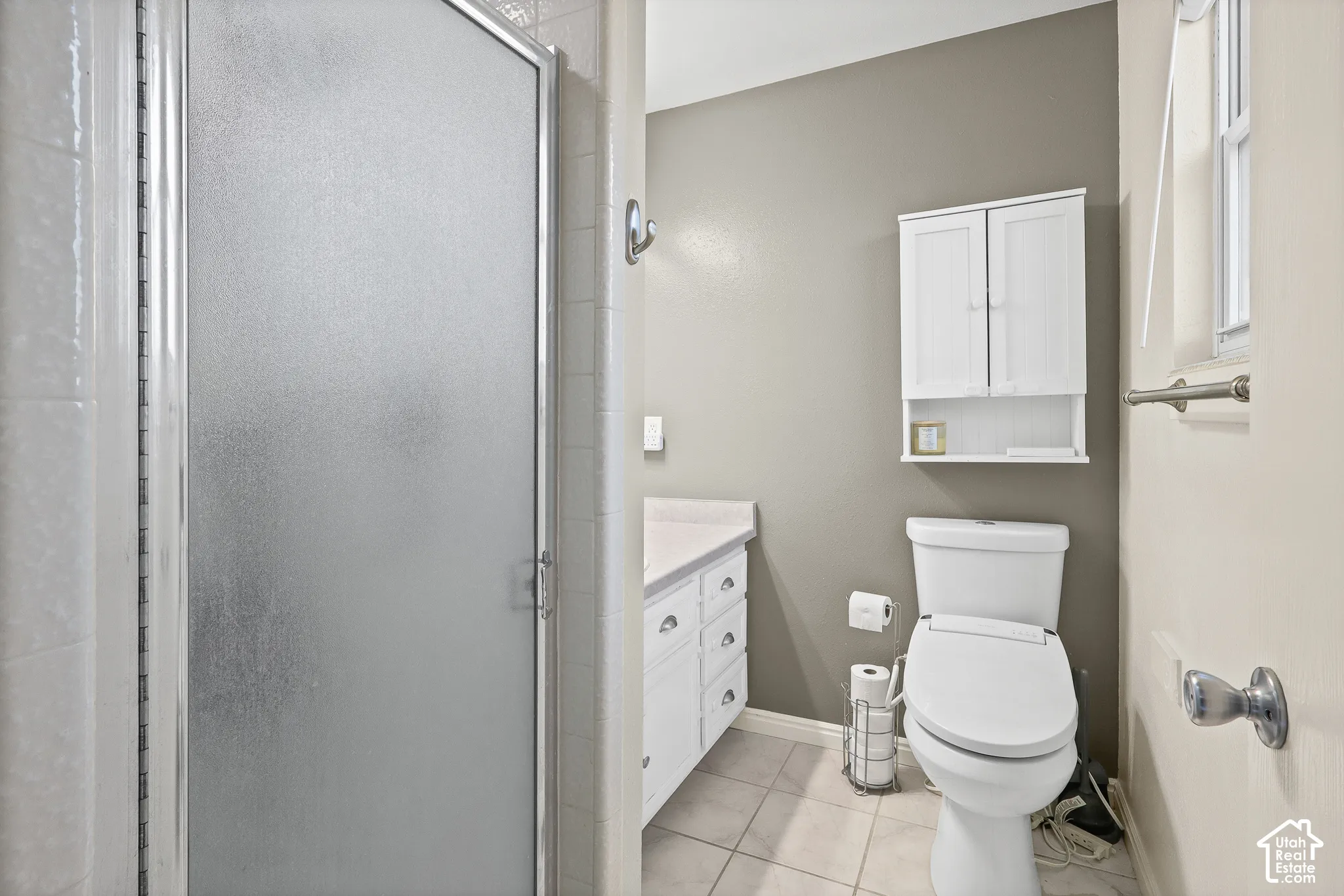 Ensuite bathroom featuring shower stall with frosted glass door, white vanity with stone-composite countertop, wall-mounted white storage cabinet, and ceramic tile flooring