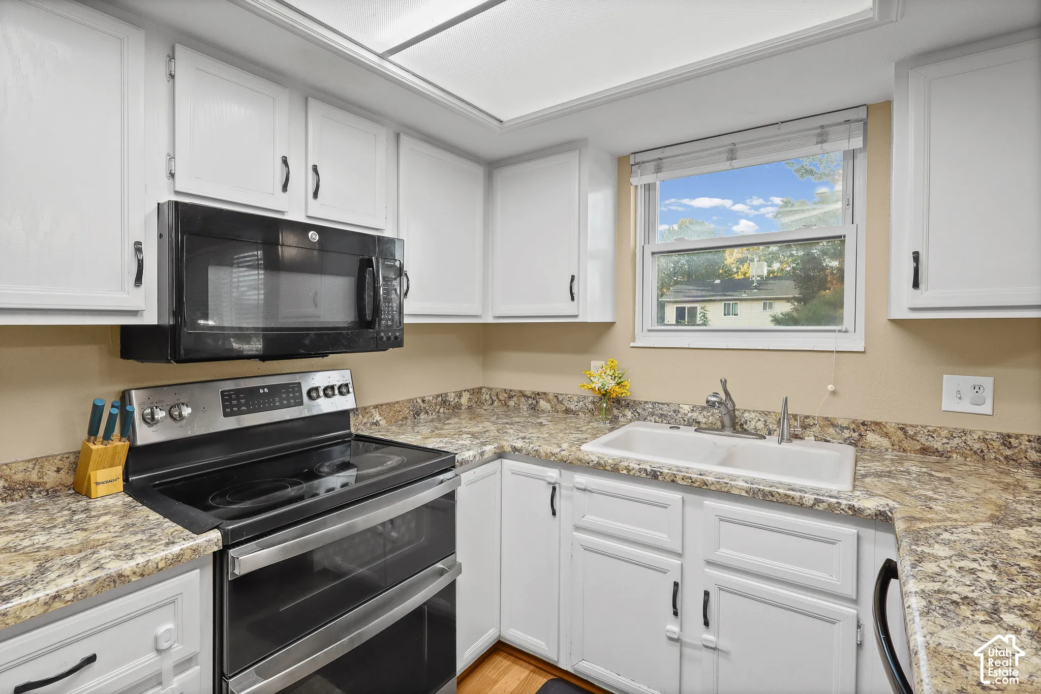 Kitchen featuring white shaker-style cabinetry, stone-patterned laminate countertops, double-basin sink, and integrated stainless steel and black appliances