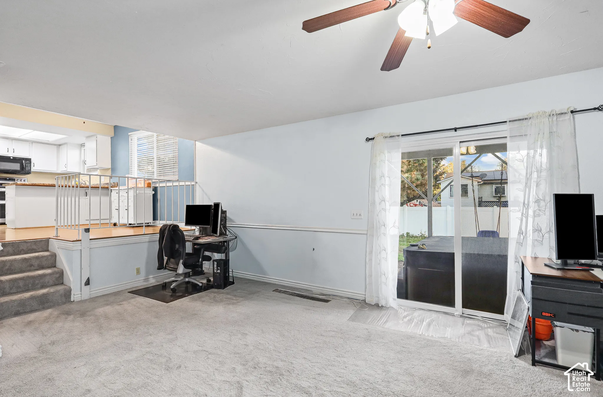 Family room featuring carpeted flooring, a ceiling fan with integrated lighting, a raised platform area with a metal railing, and sliding glass doors