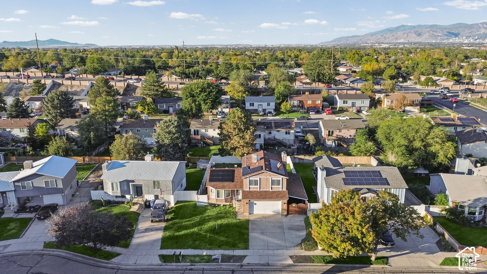 Aerial perspective of a multi-story residence featuring a two-car garage, roof-mounted solar panels, paved driveway, and grass lawn