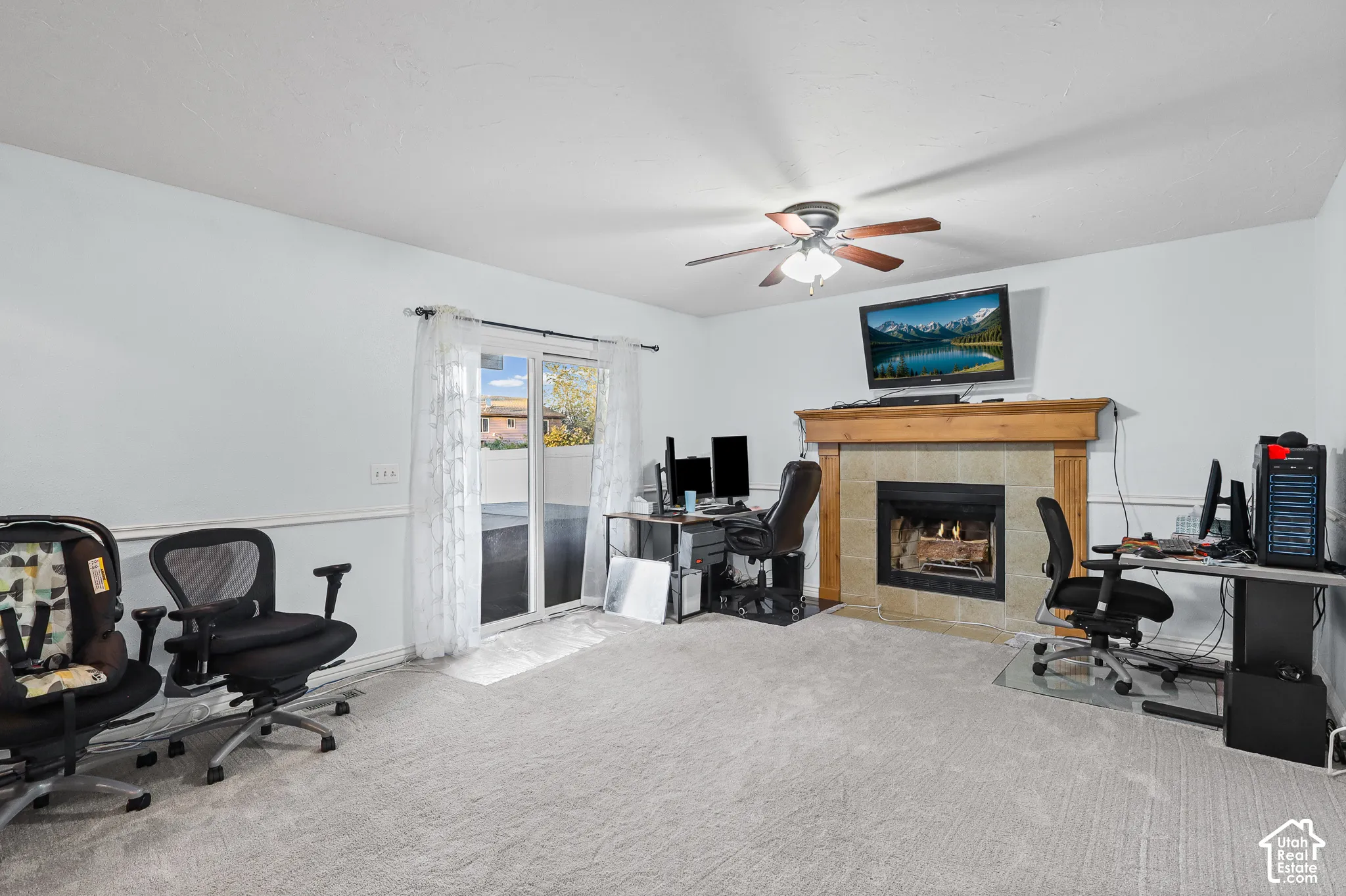 Fireplace in family room featuring a stone surround and wood mantel, sliding glass door, and a ceiling fan with integrated lighting