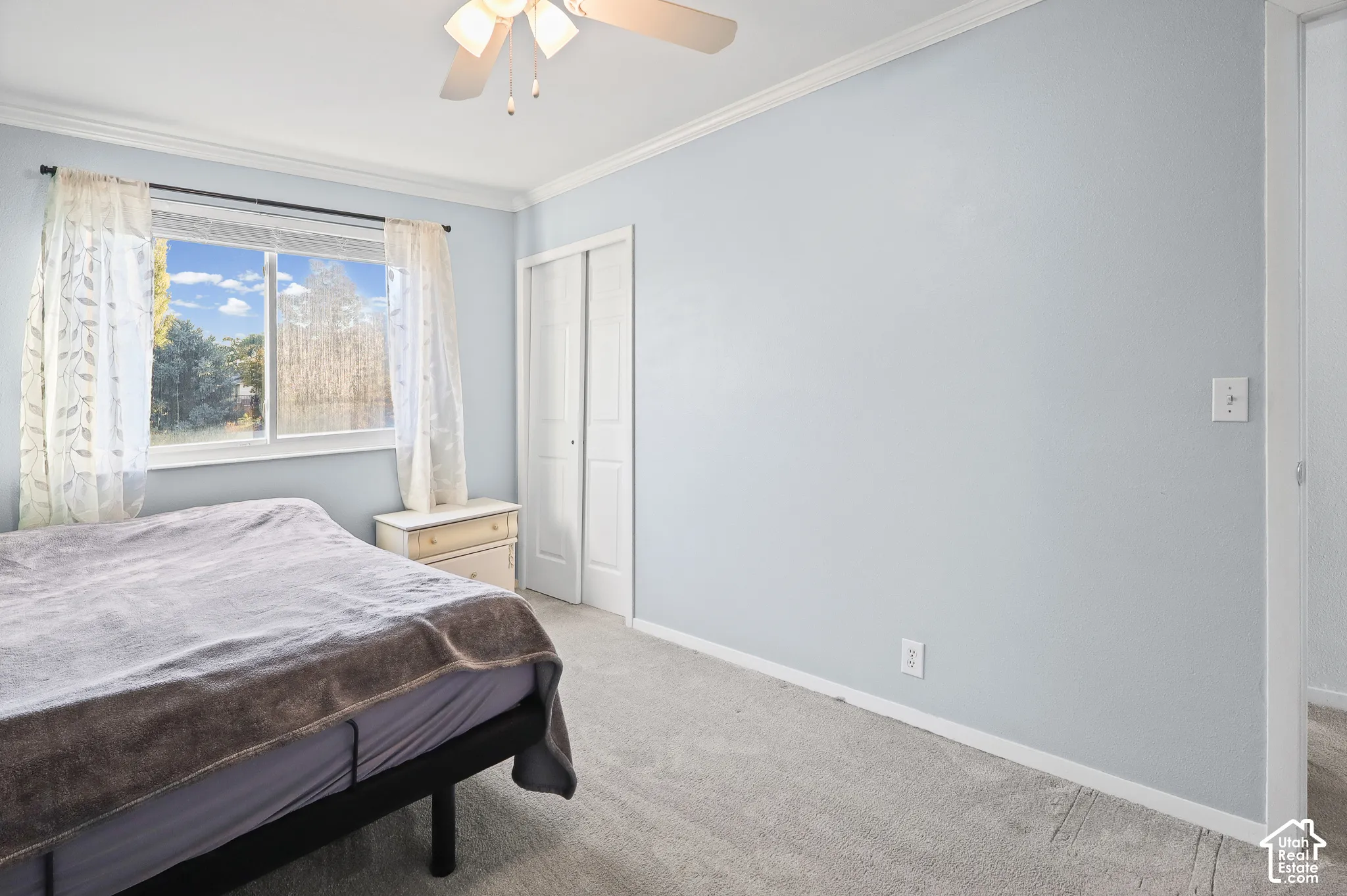 Neutral-toned bedroom with wall-to-wall carpeting, sliding closet doors, a white ceiling fan with integrated lighting, and a window with exterior scenery