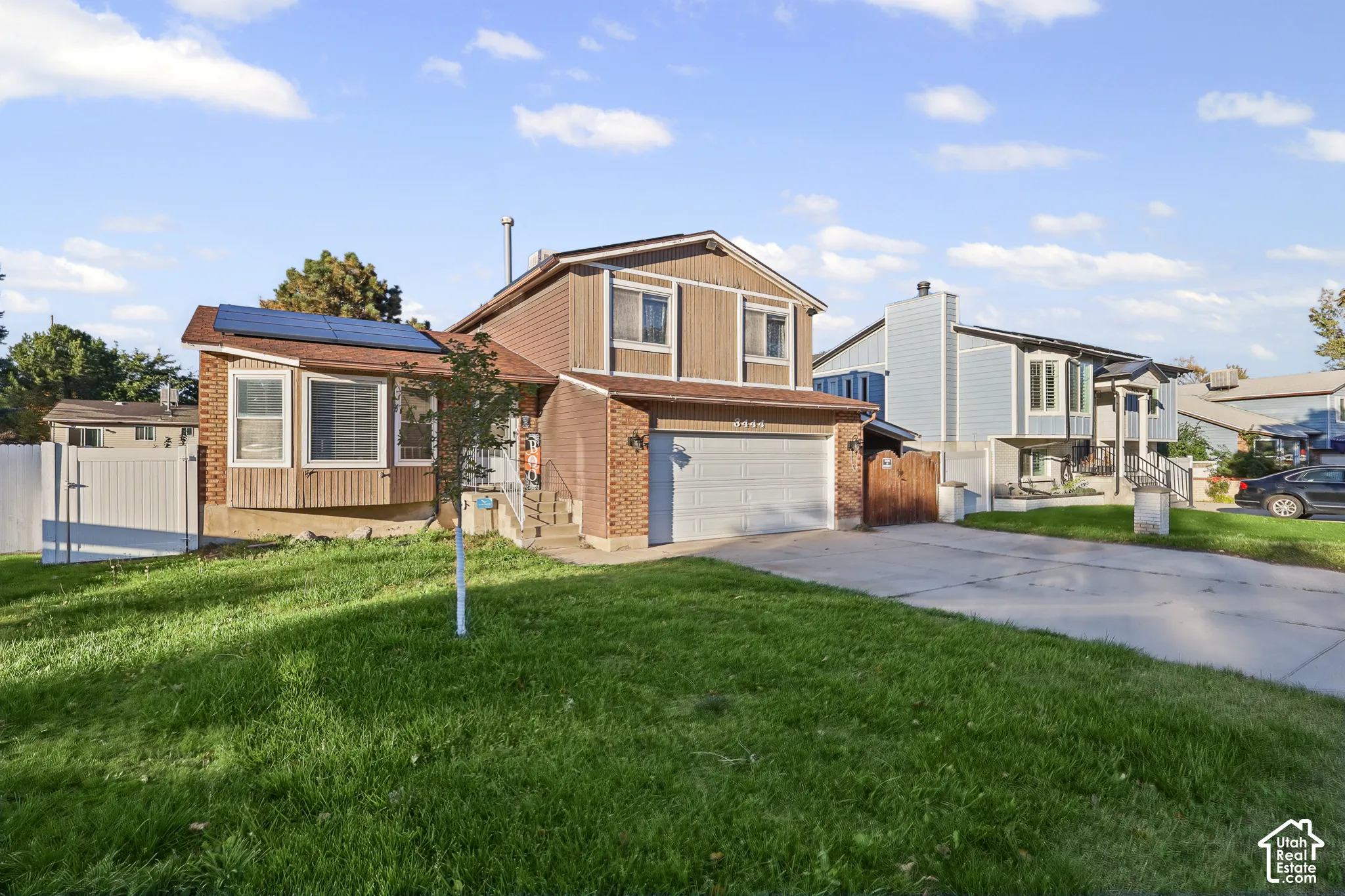 Split-level exterior featuring brick and siding facade, two-car garage, roof-mounted solar panels, and white vinyl privacy fencing