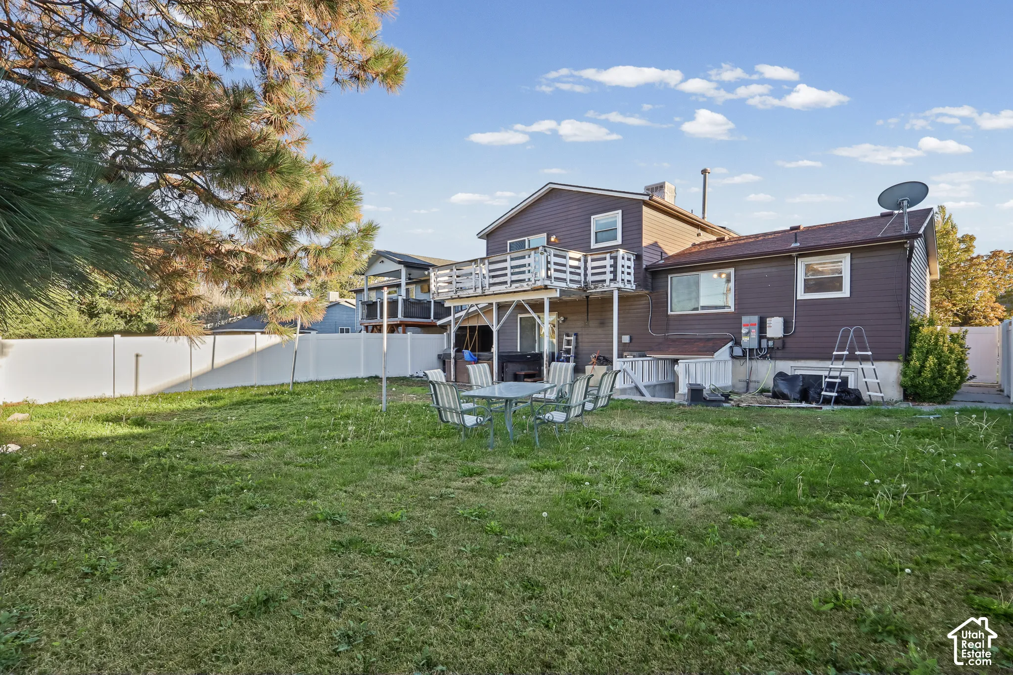 Rear exterior featuring a second-story wooden deck, white vinyl privacy fencing, mature trees, and a spacious lawn