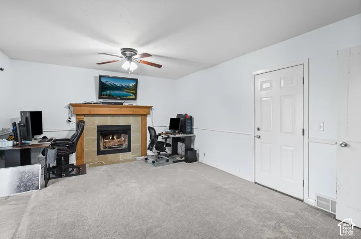 Family room with fireplace with stone-style surround and wood mantel, ceiling fan with integrated lighting, wall molding, and interior door