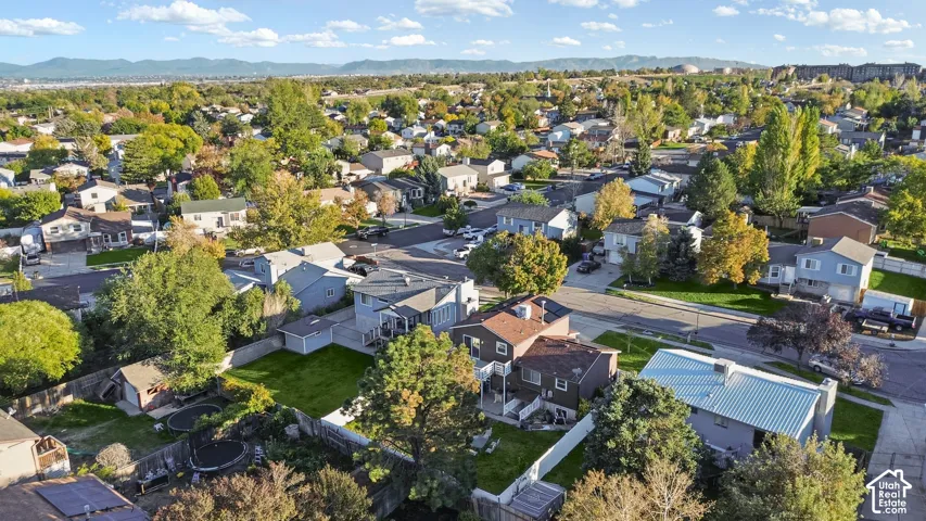 Aerial perspective featuring a multi-level residence, expansive fenced backyard, mature trees, and mountainous horizon