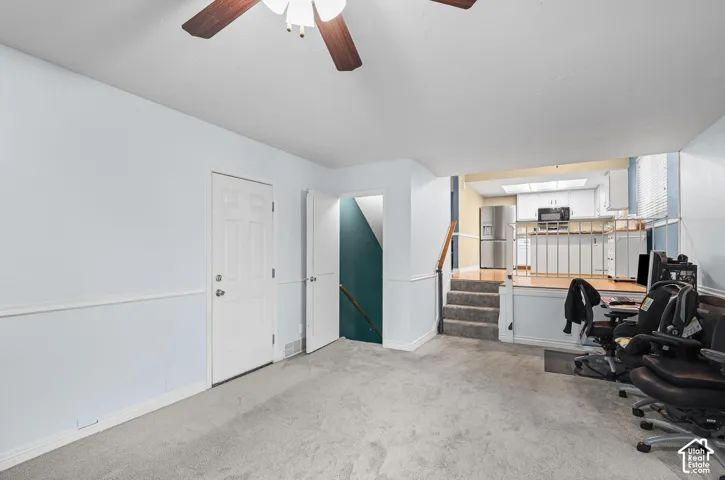 Family room featuring a ceiling fan, carpeted flooring, chair rail molding, and white cabinetry in the kitchen area