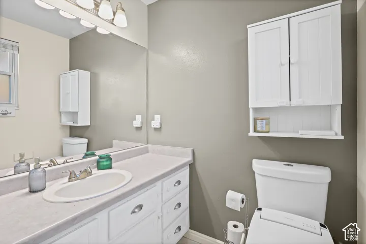 Ensuite bathroom vanity featuring white cabinetry, a molded sink, and a solid-surface countertop, complemented by a large wall-mounted mirror, multi-bulb overhead lighting, and built-in white wall cabinetry
