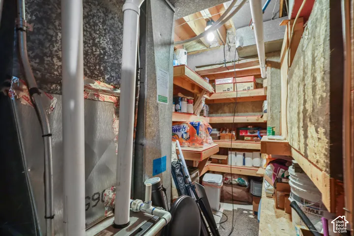 Utility space featuring a forced-air furnace unit, exposed structural beams, and wooden plank shelving