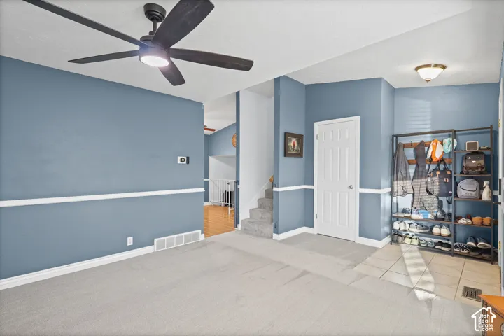 Living room space featuring grey wall-to-wall carpeting, white chair rail molding, matte black ceiling fan with integrated lighting, and a tiled entryway