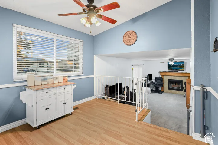 Vaulted ceilings, wood-finish flooring, metal railing, multi-pane window with horizontal blinds, and a fireplace with a wood mantel