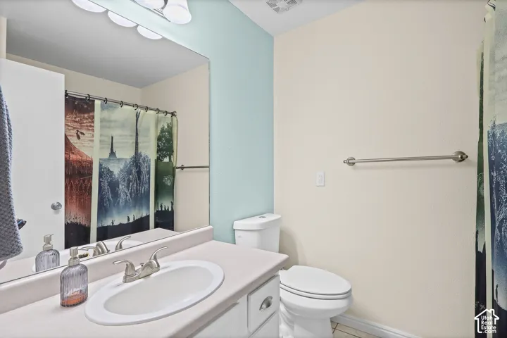 Bathroom featuring a vanity with a white integrated oval sink, chrome two-handle faucet, full-width wall mirror, multi-light fixture, and ceramic toilet