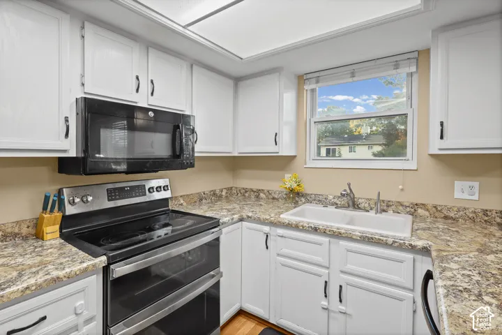 Kitchen featuring white shaker-style cabinetry, stone-patterned laminate countertops, double-basin sink, and integrated stainless steel and black appliances