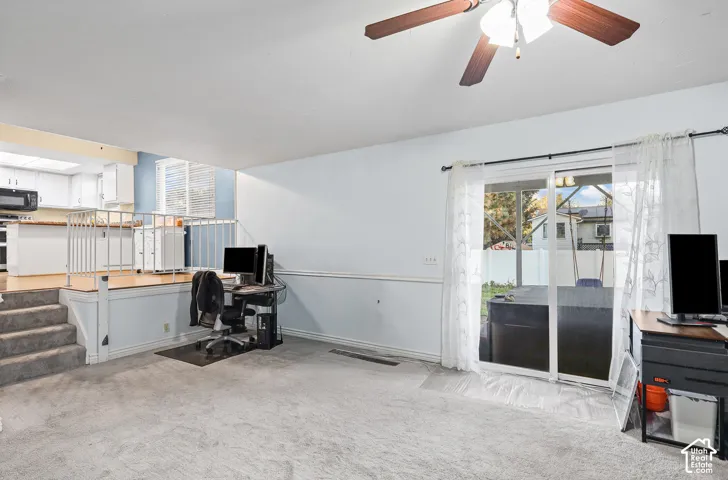 Family room featuring carpeted flooring, a ceiling fan with integrated lighting, a raised platform area with a metal railing, and sliding glass doors