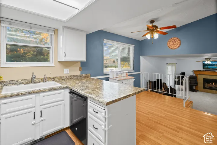 Kitchen featuring stone-finish countertops, white cabinetry, wood-finish flooring, a ceiling fan, and a fireplace with tile surround