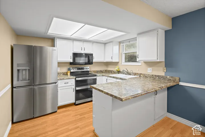 Kitchen featuring white cabinetry, stone-patterned countertops, wood-finish flooring, stainless steel refrigerator, and recessed lighting