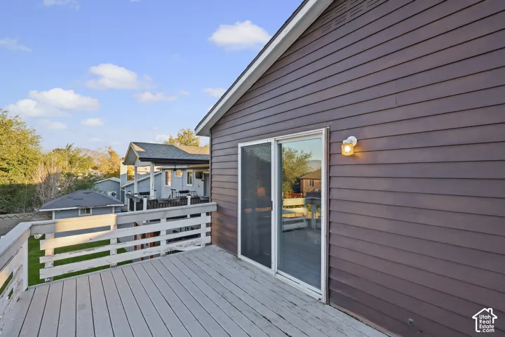 Elevated wooden deck featuring horizontal plank railings and sliding glass door access to the exterior, complemented by dark-toned horizontal siding and an attached wall-mounted light fixture
