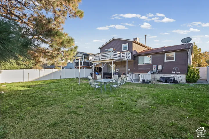 Rear exterior featuring a second-story wooden deck, white vinyl privacy fencing, mature trees, and a spacious lawn