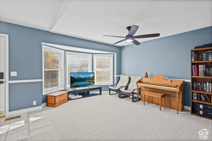 Spacious living room featuring a bay window, chair rail molding, ceiling fan with integrated lighting, and neutral carpeting