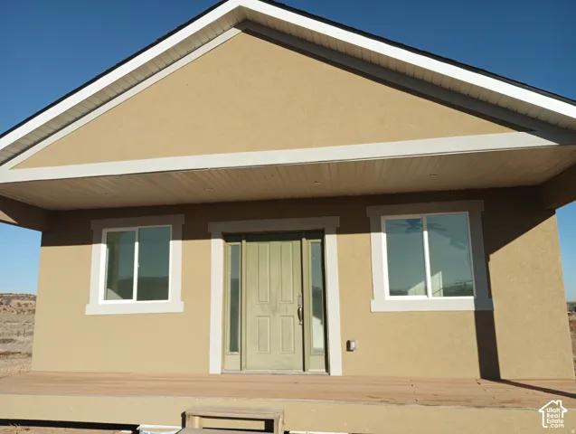Stucco exterior featuring a covered front porch, gabled roofline, recessed lighting, and a front door with dual sidelights