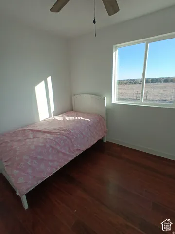 Room featuring wood-finish flooring, a large sliding window, and a ceiling fan