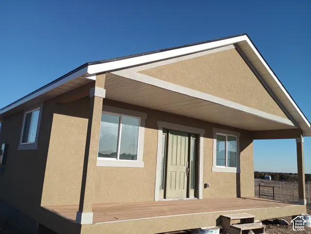 Stucco exterior featuring a covered front porch, composite decking, and a paneled entry door